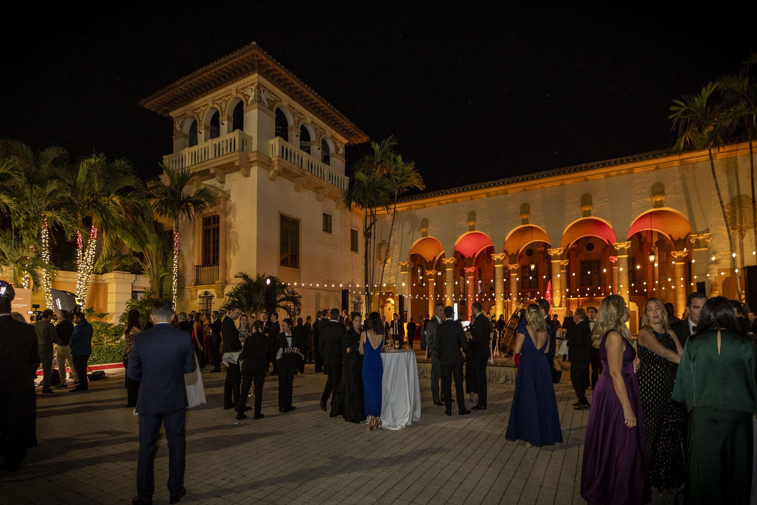 Guests attending an elegant Miami Business networking gala at a historic venue, hosted under the palm trees and evening lights.